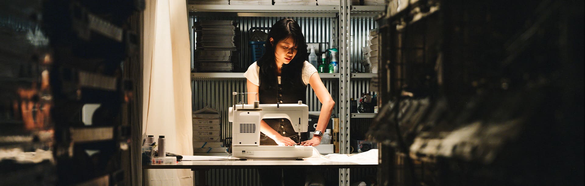 A woman with black hair and a black waistcoat works at a sewing machine