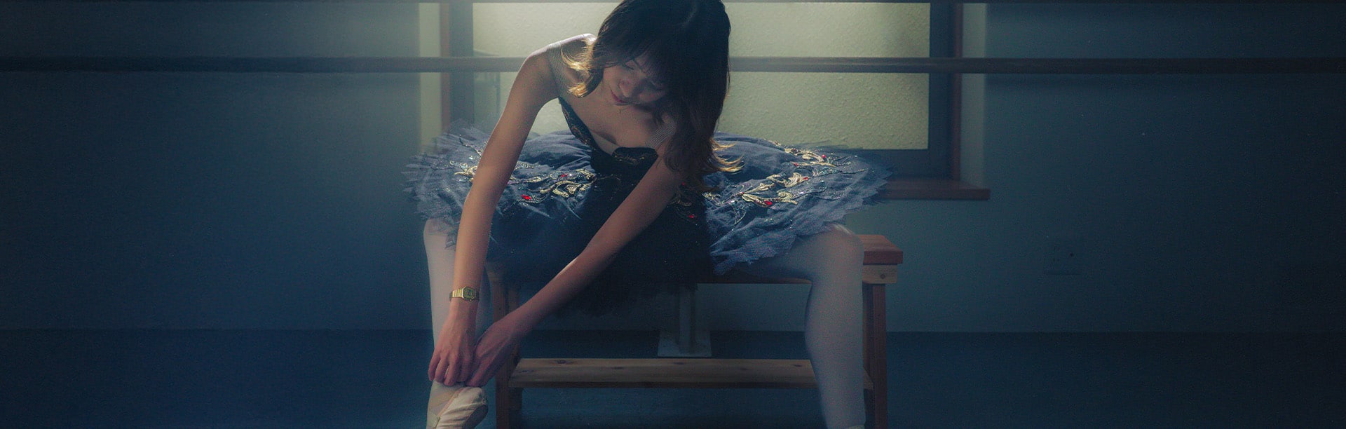A ballet dancer sits on a wooden bench and straightens her ballet shoes, wearing the gold-colored digital watch LA670WG-9 from CASIO on her wrist