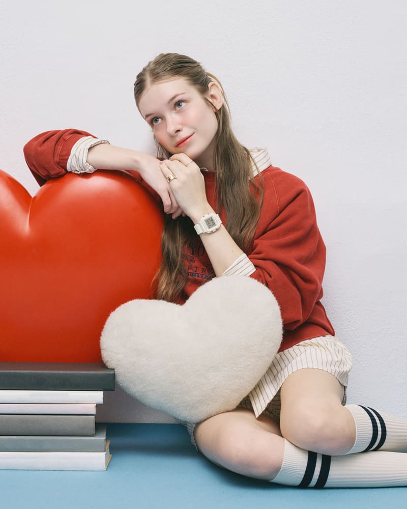 BGD-10KH-7 on the wrist of a girl wearing red clothing is leaning against a red heart-shaped cushion