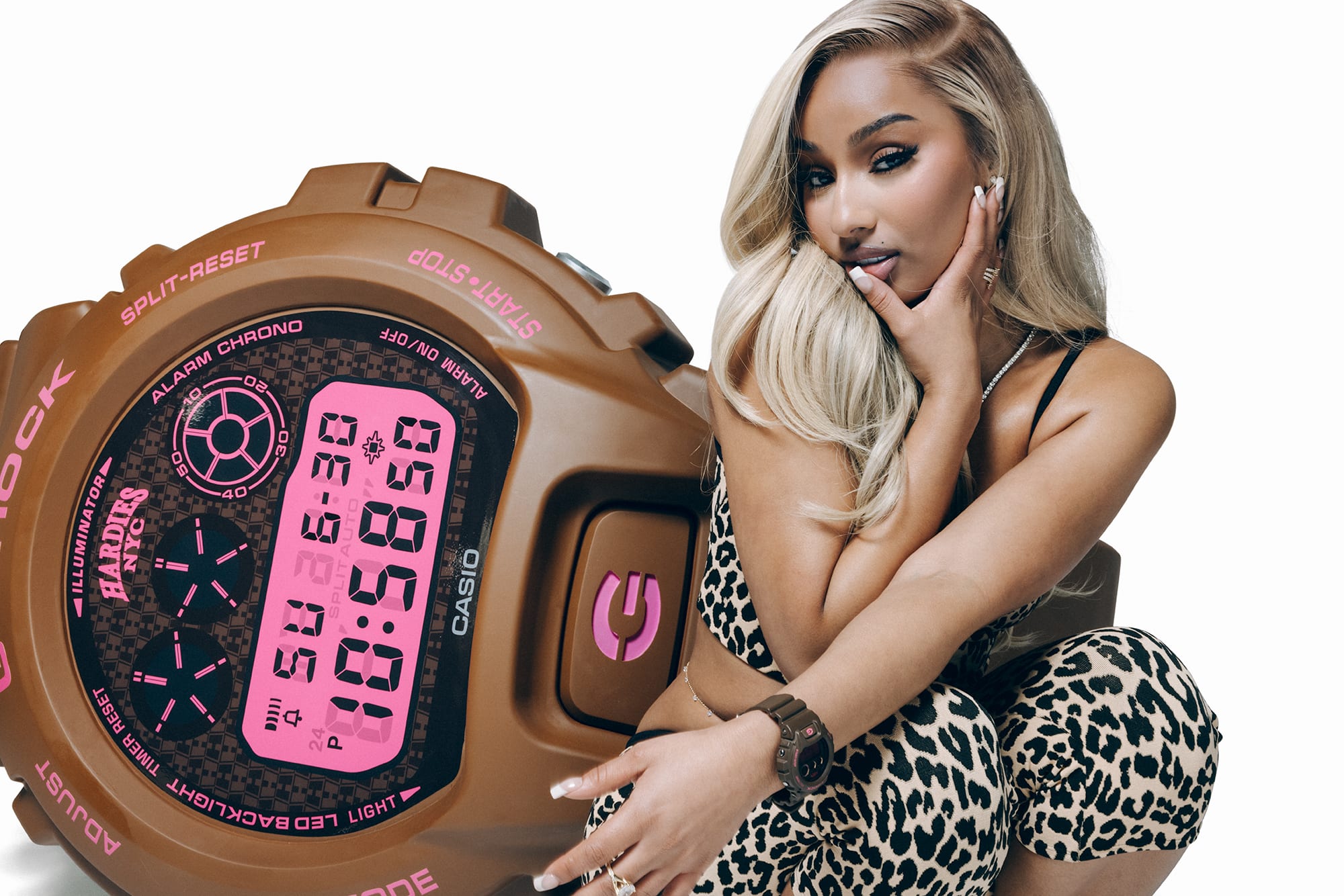 Een vrouw in luipaardprint hurkt met een bruin Casio G-Shock DW-6900HH-5 digitaal horloge om haar pols voor een grote close-up van het horloge met roze displayverlichting