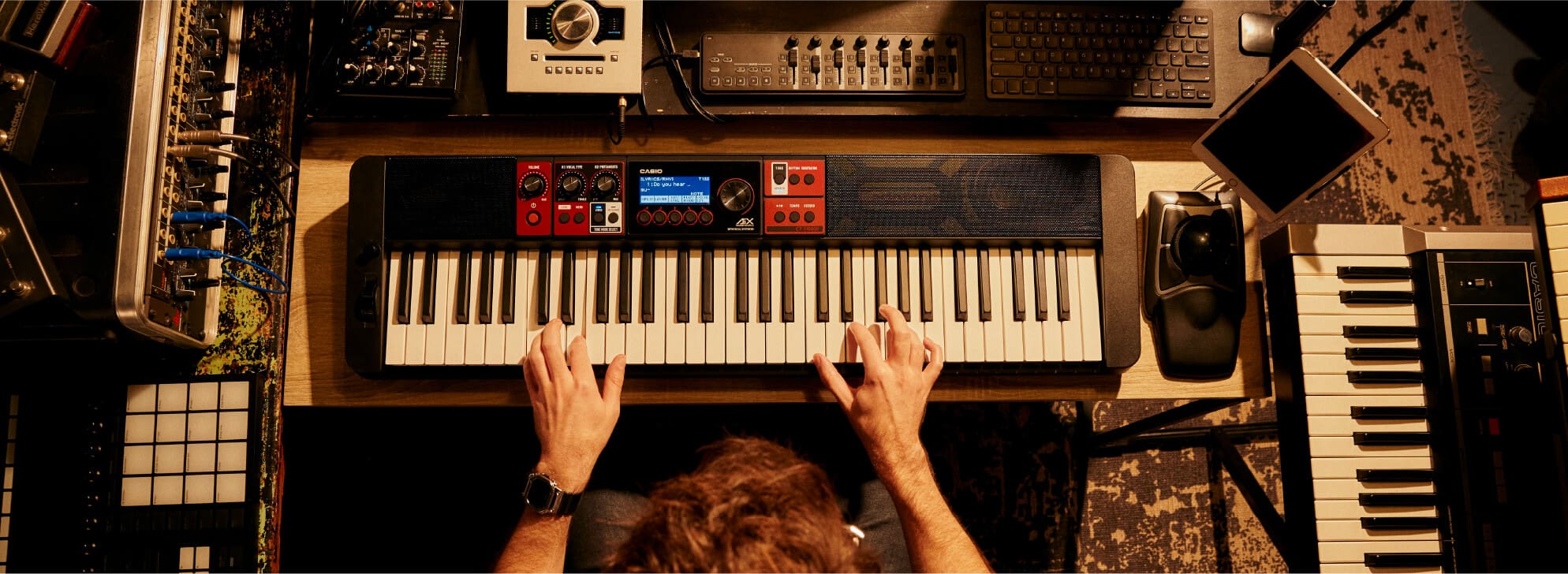 Casiotone keyboard in vogelvlucht op een bureau met laptop en mixer, iemand bespeelt het keyboard