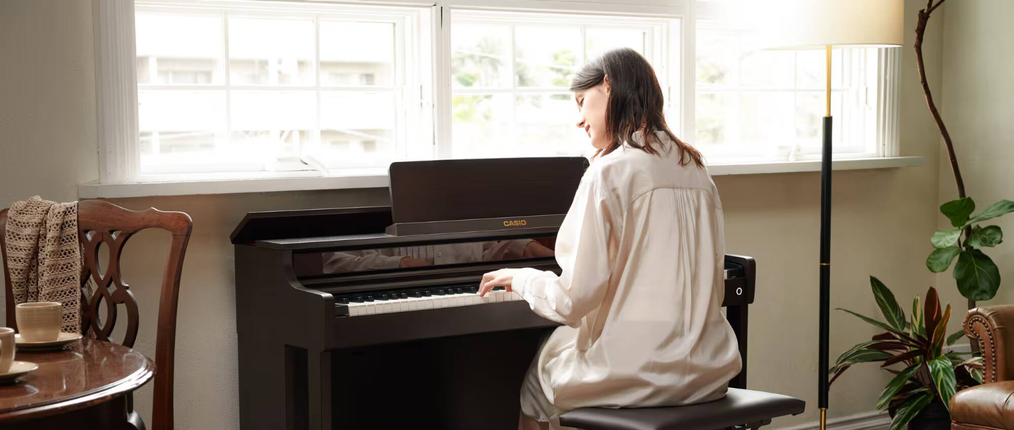 Een vrouw zit aan een zwarte Casio-piano en speelt.