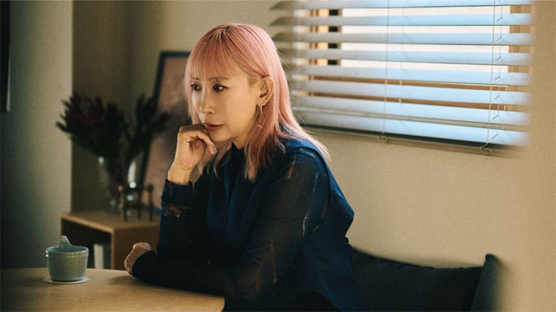 Mika Ninagawa zit aan een tafel. De afbeelding linkt naar de Privia Magazine Voices-pagina van Mika Ninagawa.