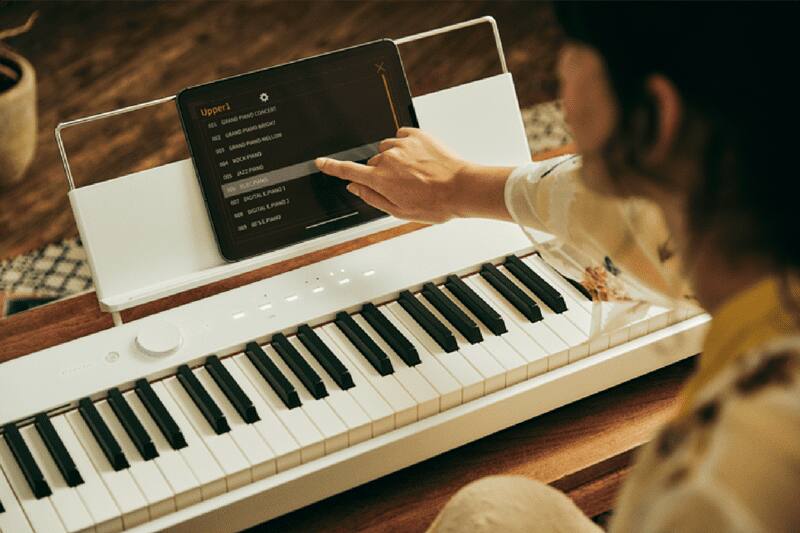 Een persoon raakt een tablet aan die in de transparante bladhouder van een witte digitale piano staat om de Casio Music Space-app te bedienen.