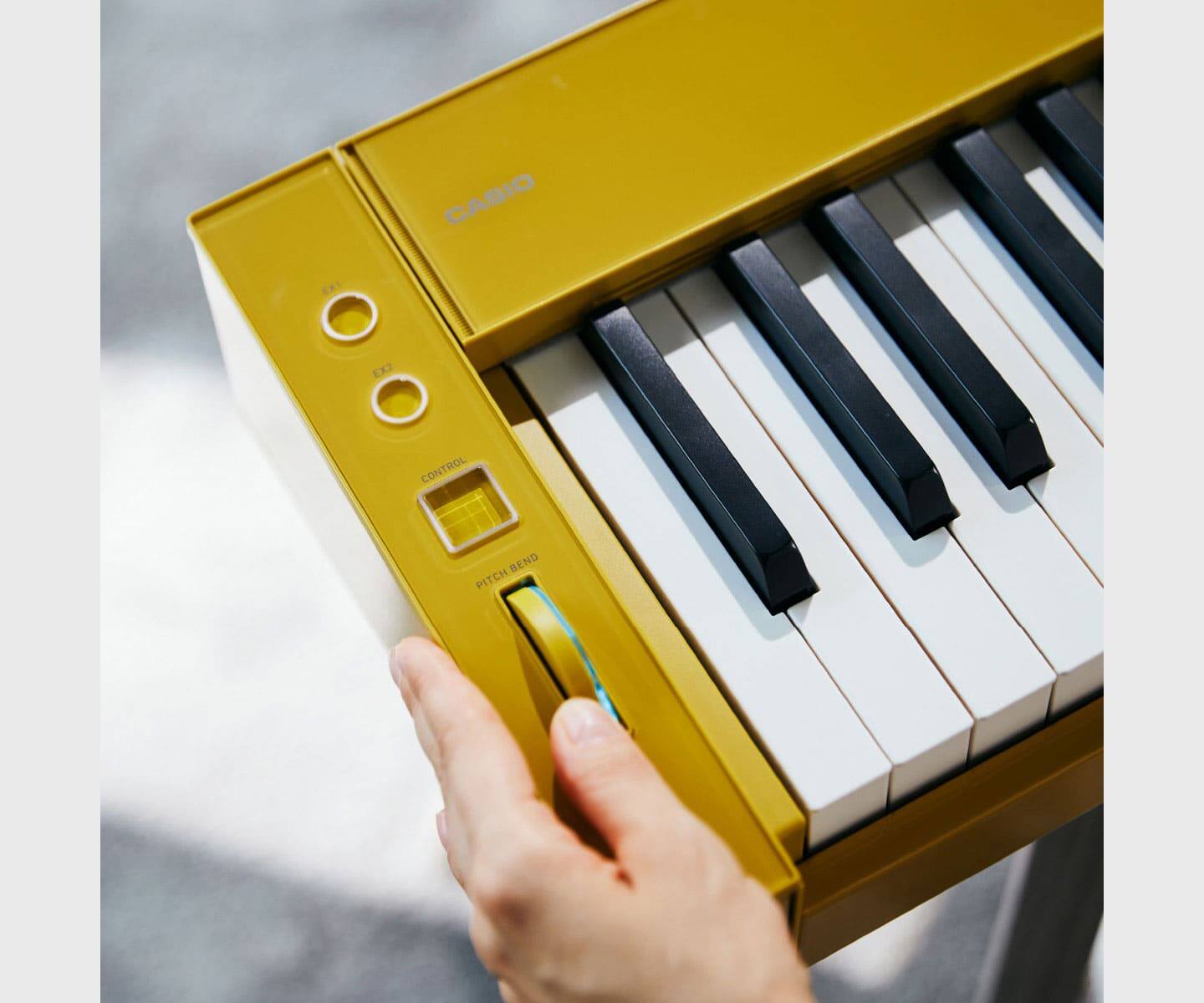 Close-up van draaiknoppen en toetsen aan de linkerkant van de gele PX-S6000 digitale piano