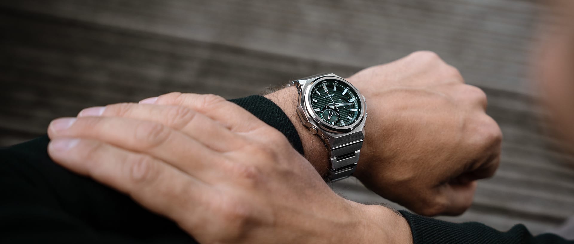 Het G-SHOCK G-Steel GST-B1000 horloge met een zilveren band, een donkergroene analoge lunette en witte indexen om de pols van een man.