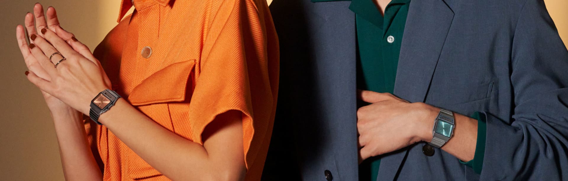 Een vrouw in oranje kleding draagt de AQ-800ECG met oranje wijzerplaat. Naast haar poseert een in het blauw geklede man met de AQ-800ECG met blauwe wijzerplaat. De afbeelding linkt naar de productpagina van het Casio vintage polshorloge AQ-800EC-2A.