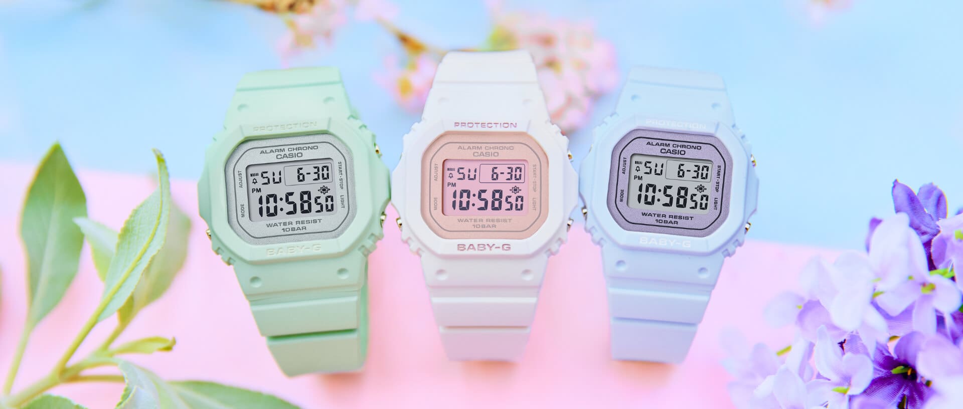 Drie Baby-G zomermodellen in pastelkleuren liggen op een kleurrijke achtergrond