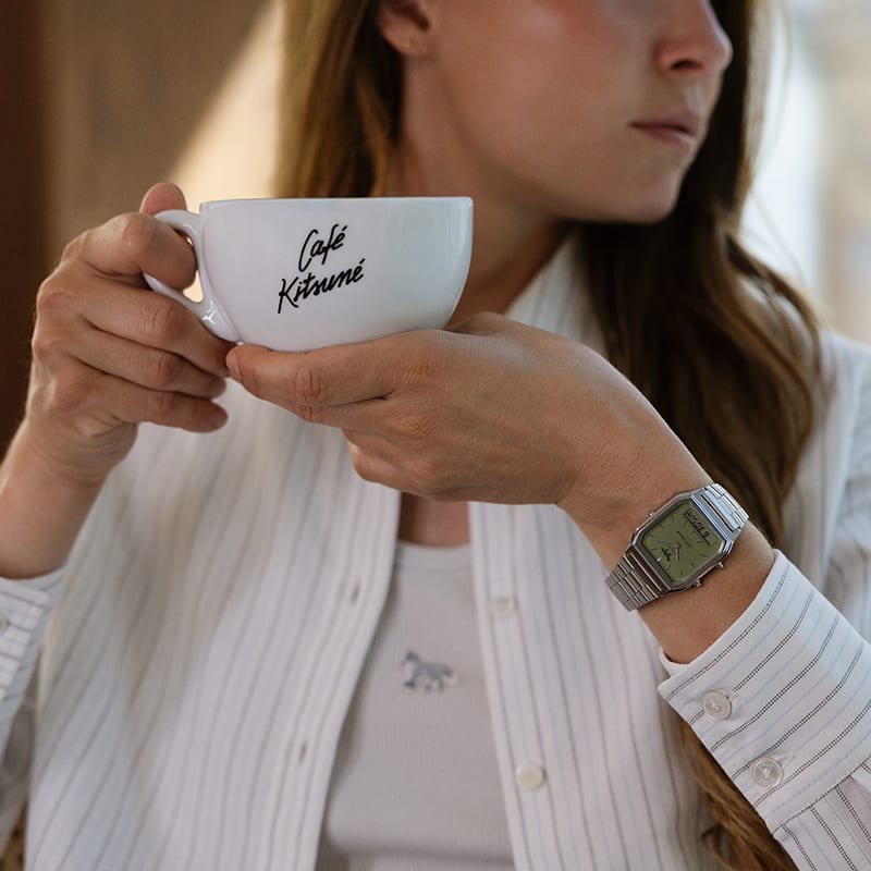 Een vrouw met een koffiemok van Café Kitsuné om, die het CASIO AQ-230ECK-3A-samenwerkingshorloge draagt.