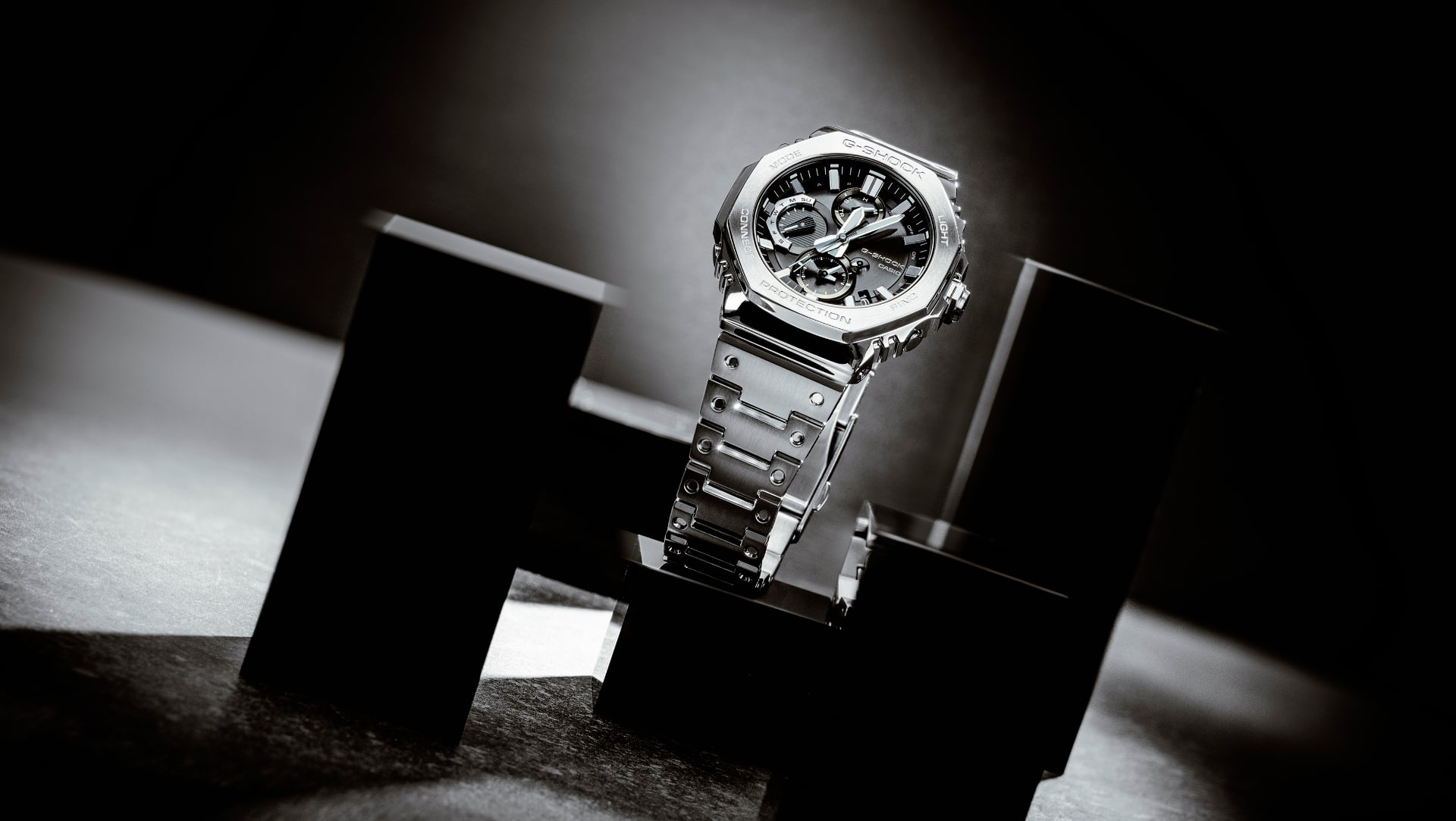 De GMC-B2100 chronograaf met zwarte wijzerplaat en zilverkleurige metalen armband op een zwart plateau.