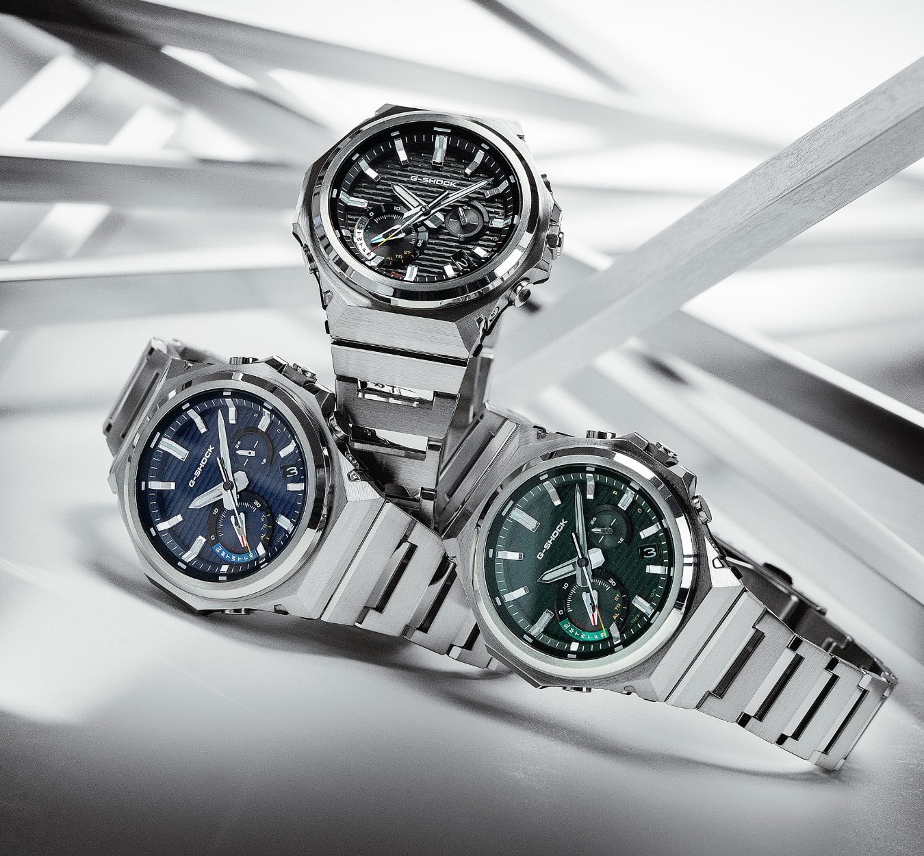 Os três relógios analógicos GST-B1000 com moldura preta, azul escura e verde escura empilhados uns sobre os outros em frente a um fundo branco.