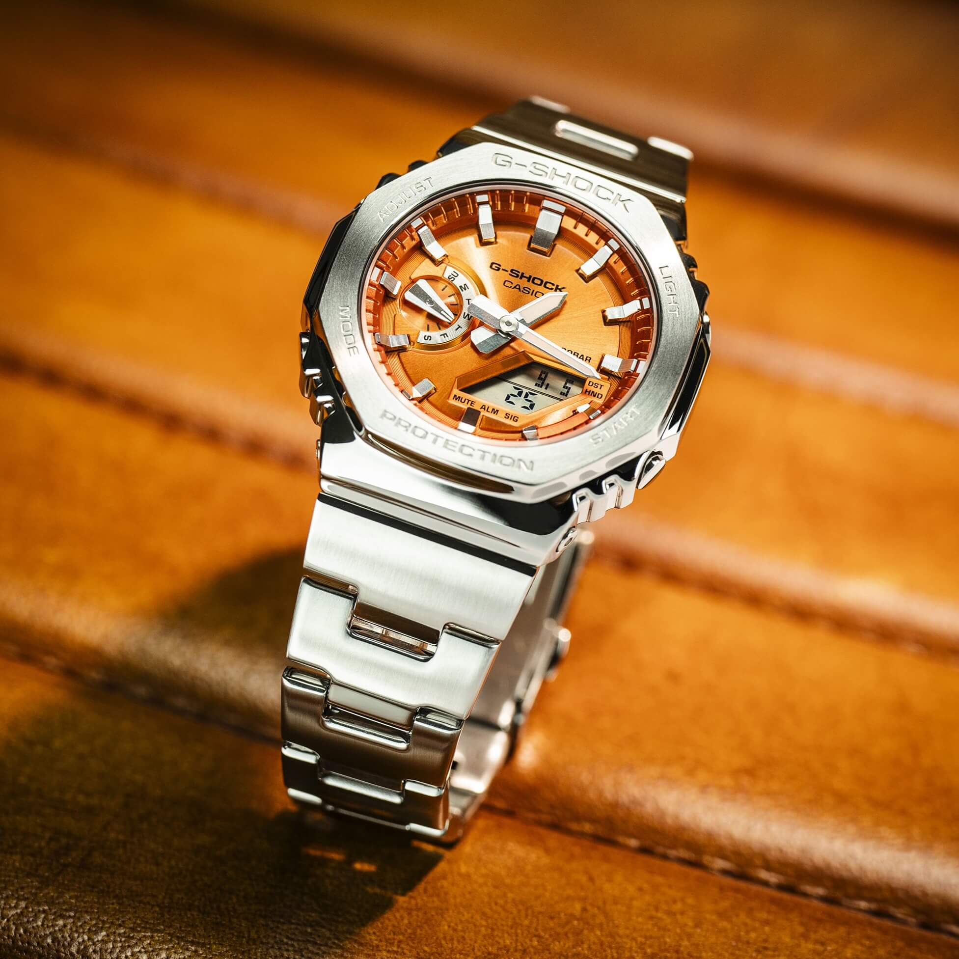 O relógio de pulso GM-2110D-4AER totalmente em metal com mostrador laranja numa cadeira de couro