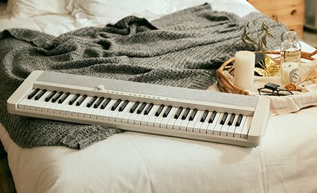 O piano digital branco CT-S1WE está deitado numa cama