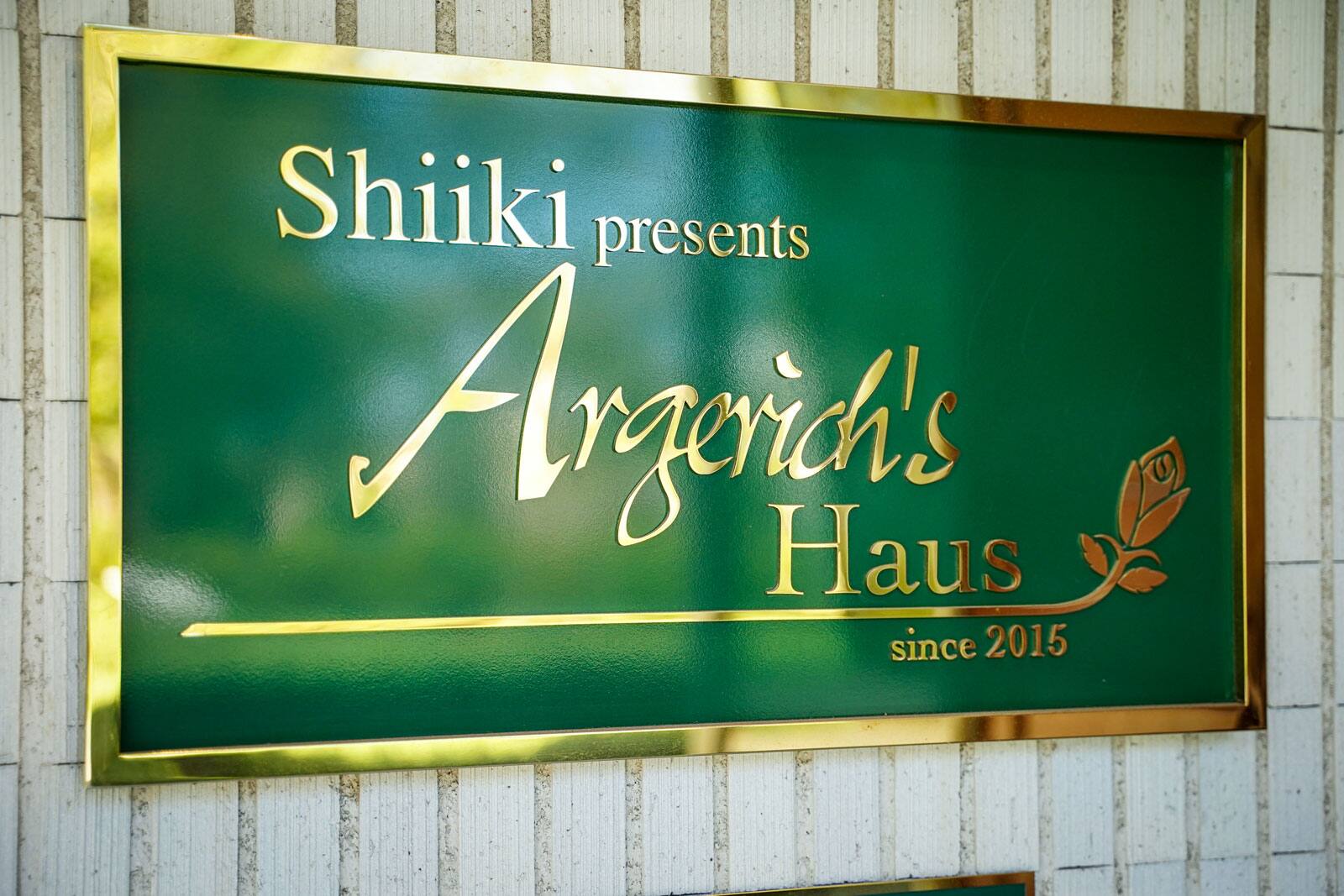 Uma placa verde com letras douradas: «Shiiki presents Argerich's Haus»