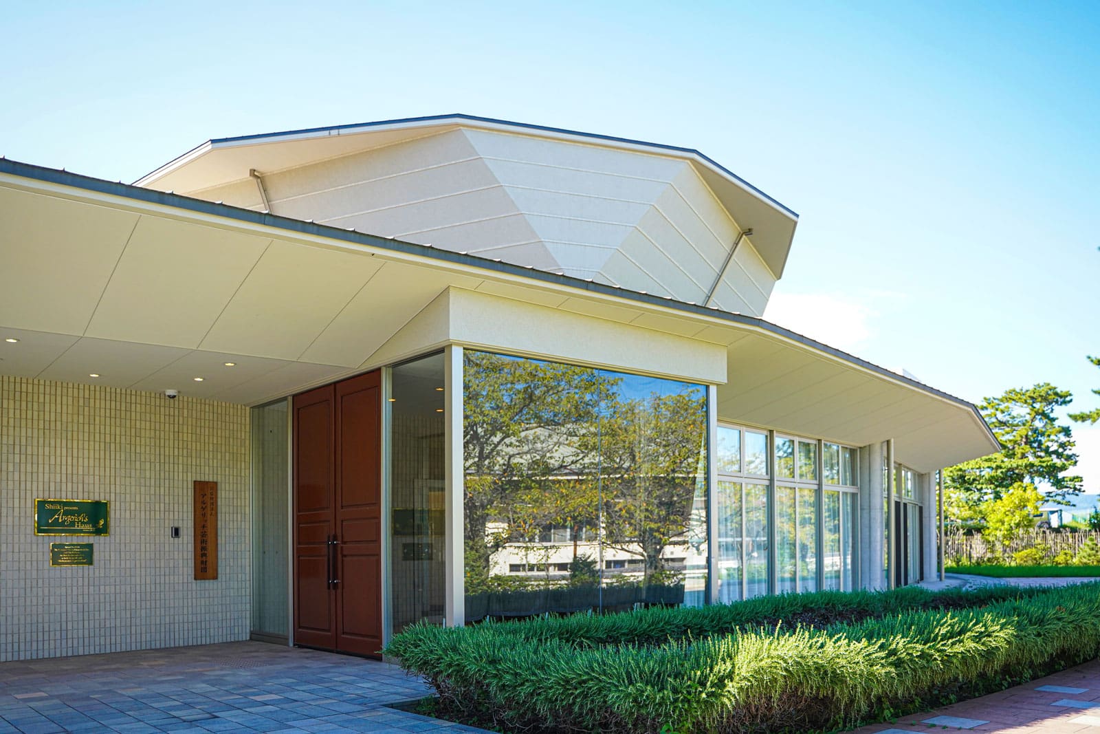 A casa de Martha Argerich, com uma grande fachada envidraçada e um jardim à frente, sob um céu azul.