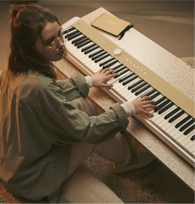 Uma jovem toca no piano digital Privia PX-S1100MB bege claro