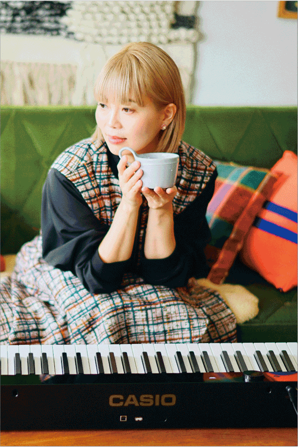A pianista Kie Katagi, de Kyoto, sentada no sofá com uma chávena na mão, em frente ao seu piano digital Privia preto. A imagem leva para a página Life with Privia dela.