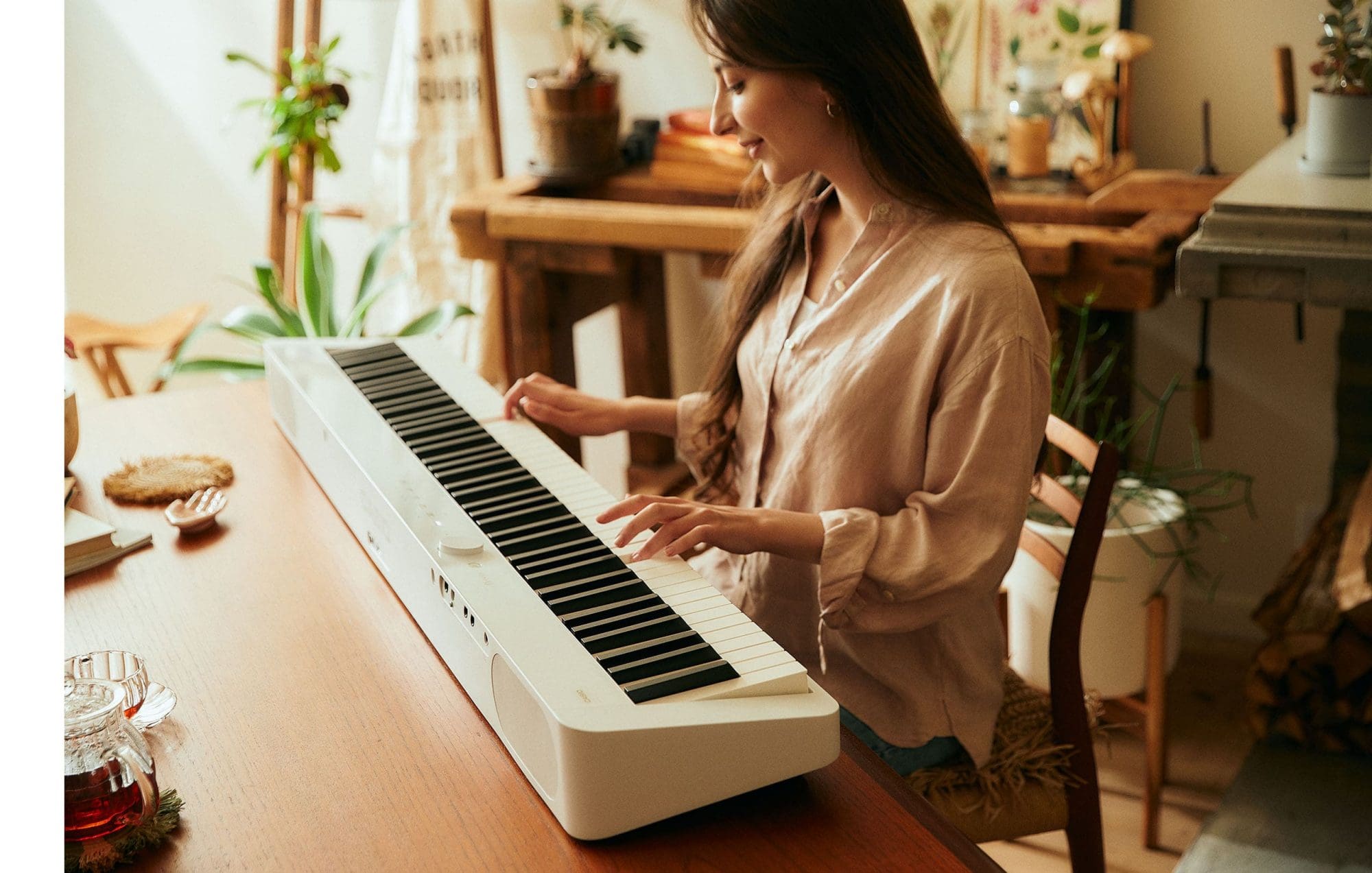 Uma mulher sentada a uma mesa de madeira a tocar um piano digital branco