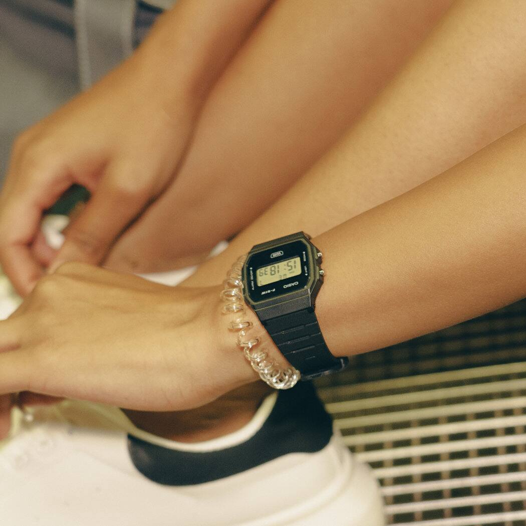 O relógio de pulso CASIO TIMELESS COLLECTION F-91WB-1AEF com mostrador digital e bracelete preta fabricada em resina de base biológica no pulso de uma modelo feminina