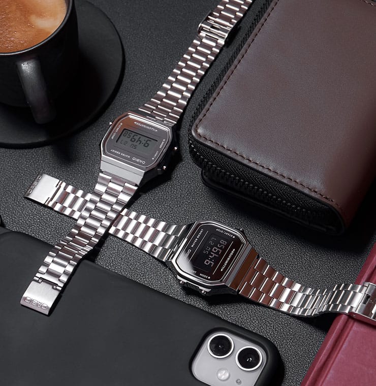 Dois relógios da "coleção icónica" CASIO Vintage estão sobre uma mesa junto a uma chávena de café