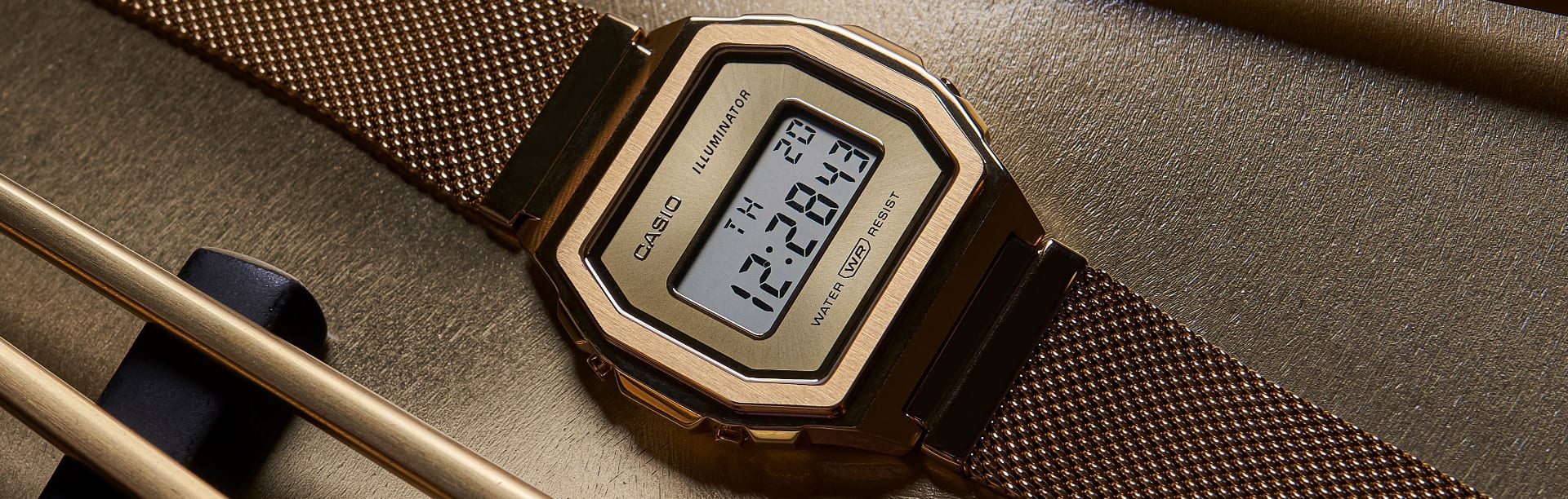O relógio digital CASIO Vintage A1000 dourado ao lado de palitos de sushi dourados