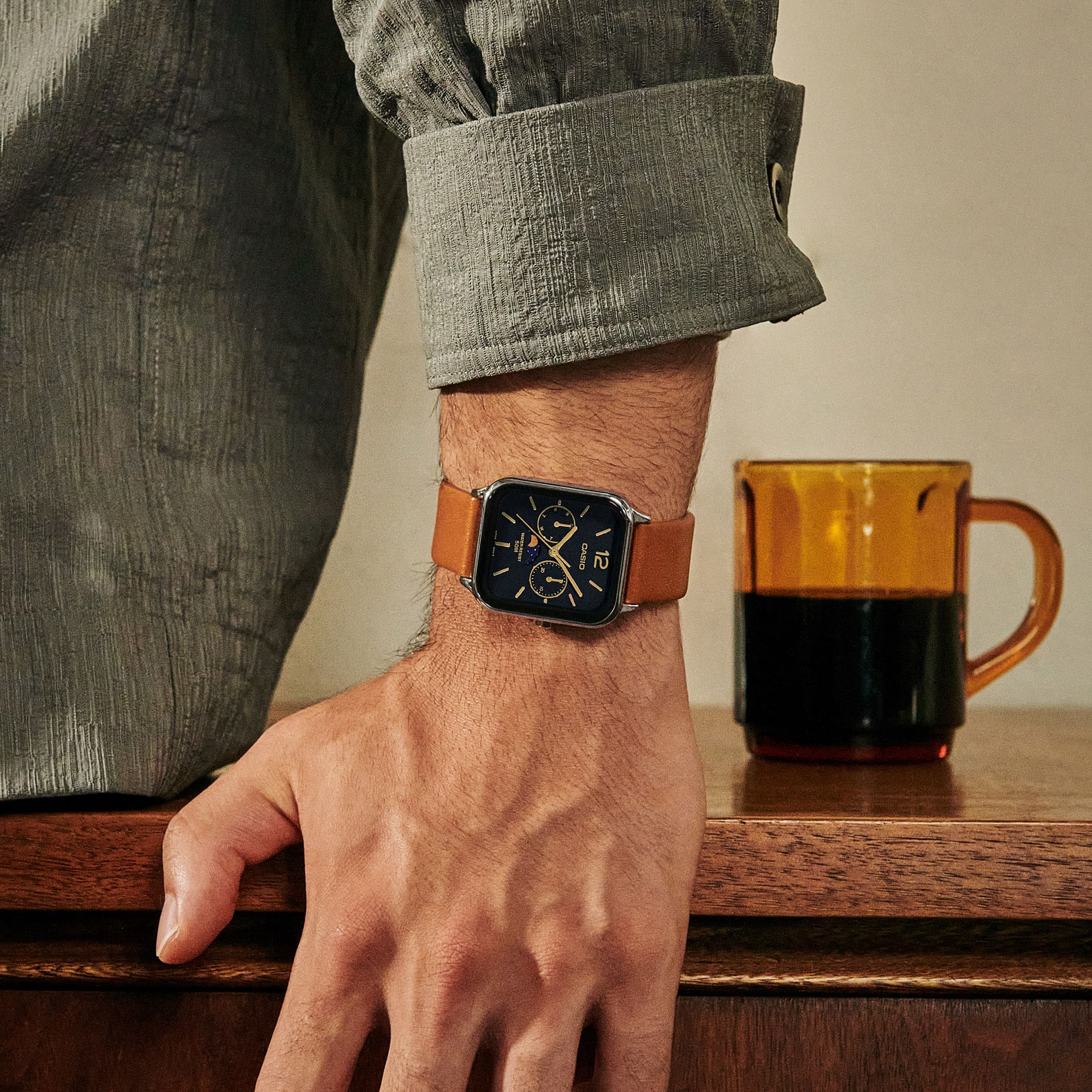O relógio de pulso analógico MTP-M305L-1AV com bracelete em pele castanha clara e mostrador preto no pulso de um homem