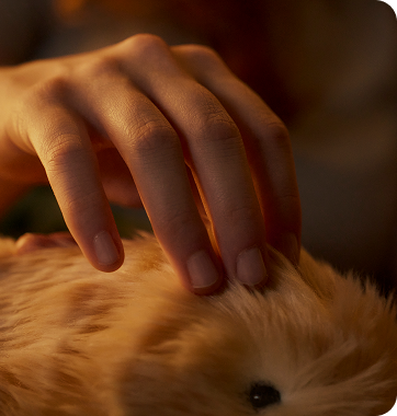 An image of a woman stroking a gold-colored Moflin in a dimly lit room.