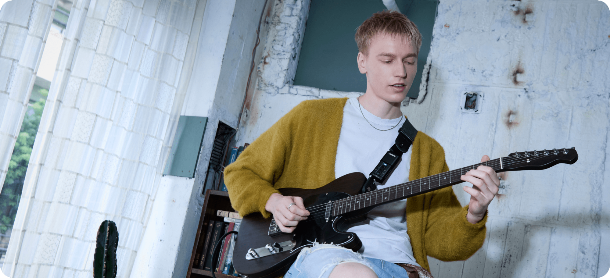 A photo of a man seated on a chair playing a guitar fitted with the DIMENSION SHIFTER.