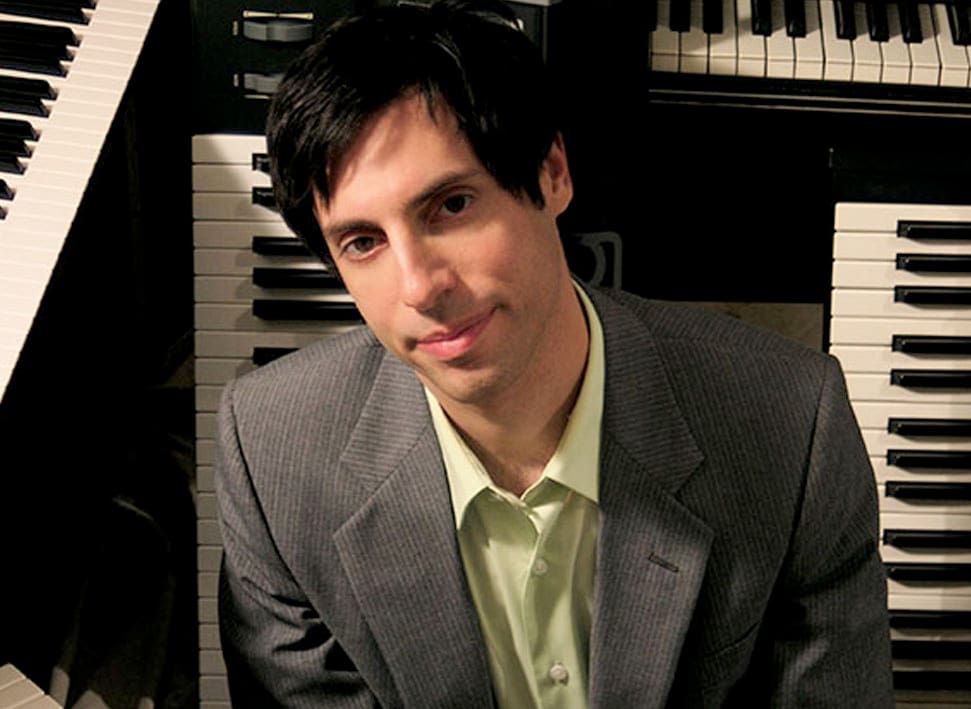 Tom Brislin Headshot With Pianos Behind Him