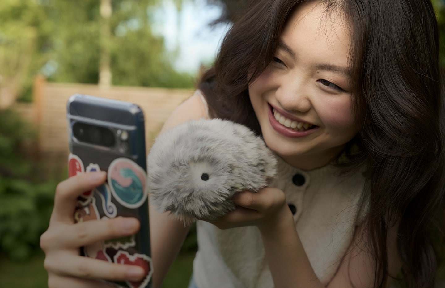 An image of a woman holding Moflin in her left hand, taking a selfie with her smartphone.