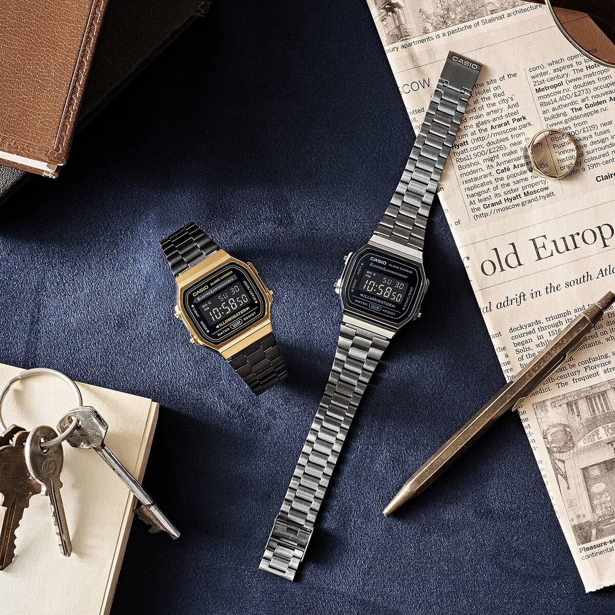 Casio Vintage A168WEGB- 1B and A168WGG-1BVT watches on a desk with keys, pen,  and newspaper denoting style