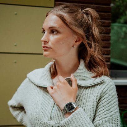 Eine Frau fasst sich mit der Hand an ihren Pulloverkragen, sie trägt die CASIO VINTAGE COLLECTION Armbanduhr ABL-100WE-1BEF mit schwarzer Lünette und silbernem Metallarmband