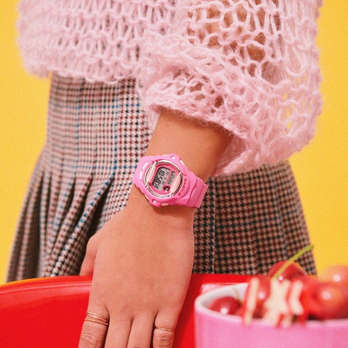 Die pinke BG-169CH-4ER am Handgelenk einer Frau. Diese trägt einen rosafarbenen Pullover und einen rot-blau karierten Rock. 