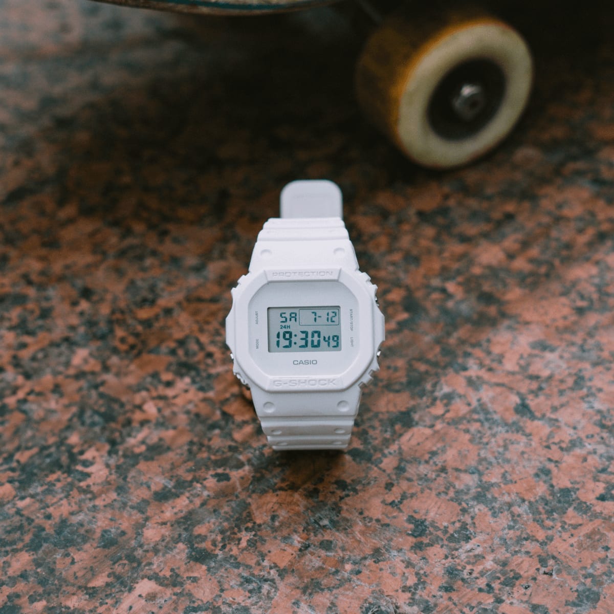 Frontansicht der DW-5600WW-7 auf einem rötlichen Steinboden. Im Hintergrund ist ein Skateboard zu sehen