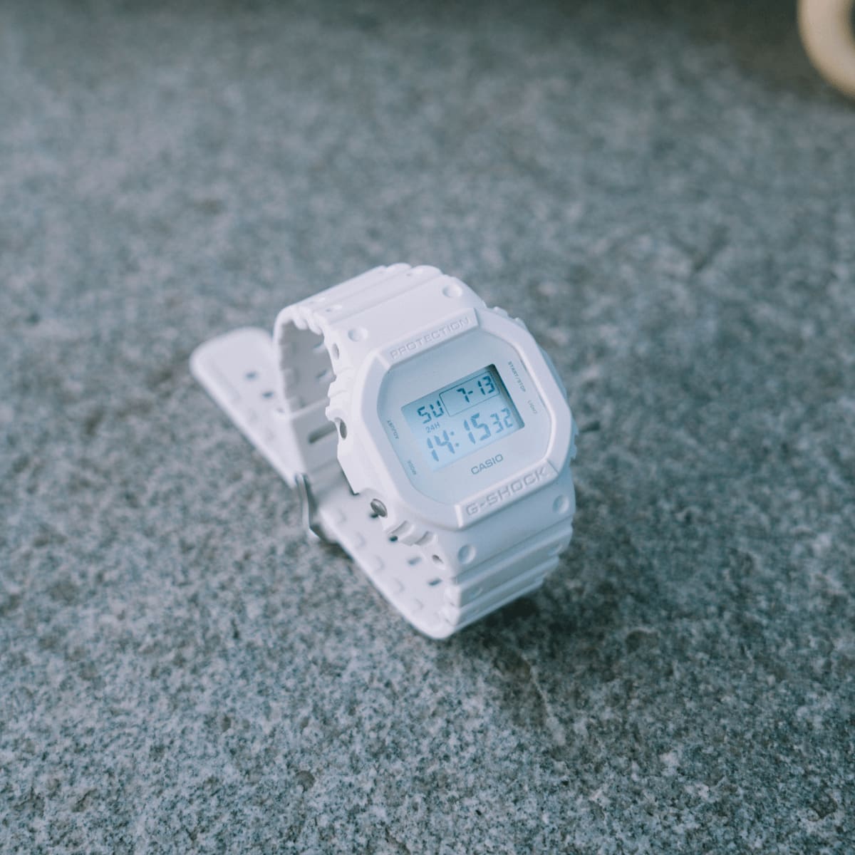 Die DW-5600WW-7 steht mit geschlossenem Armband auf einem Steinboden und ist leicht schräg von der linken Seite zu sehen