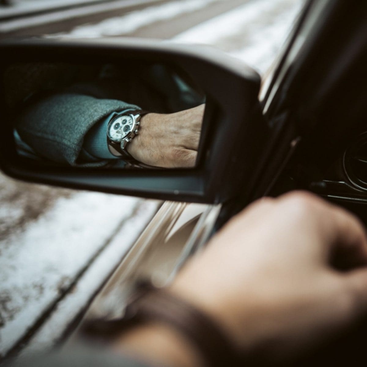 Die Chronographenuhr EFR-575 mit braunem Lederarmband am Handgelenk eines Mannes, der in einem Seitenspiegel eines Autos gesehen wird.