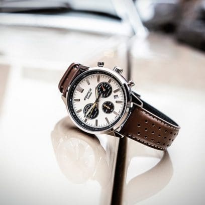 Der EDIFICE-Chronograph mit weißer Lünette und braunem Lederarmband auf der Motorhaube eines Autos.