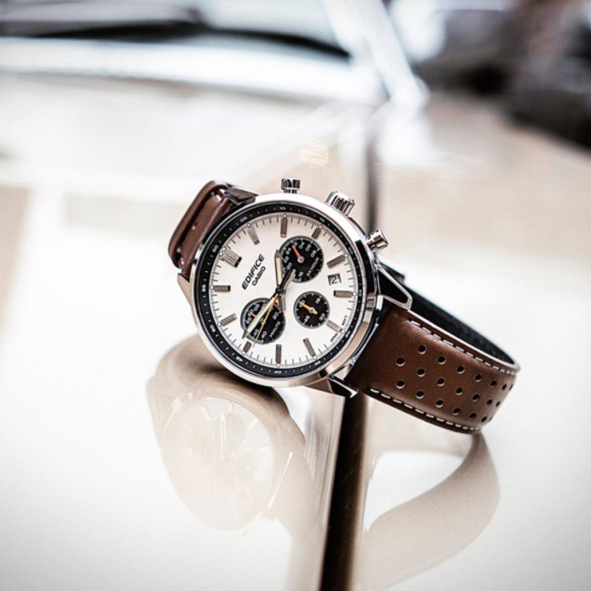 Der EDIFICE-Chronograph mit weißer Lünette und braunem Lederarmband auf der Motorhaube eines Autos.