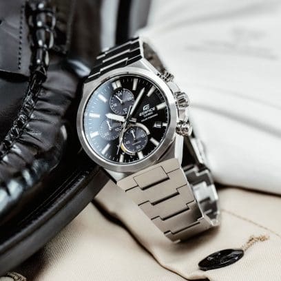 Die EFS-S630D-1AV lehnt mit geschlossenem Armband an einem schwarzen Lackschuh