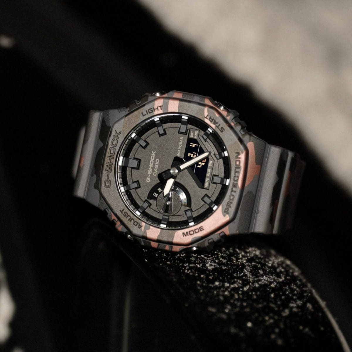 Die analog-digitale Armbanduhr GA-2100CM-8AER liegt seitlich auf einem dunklen Untergrund