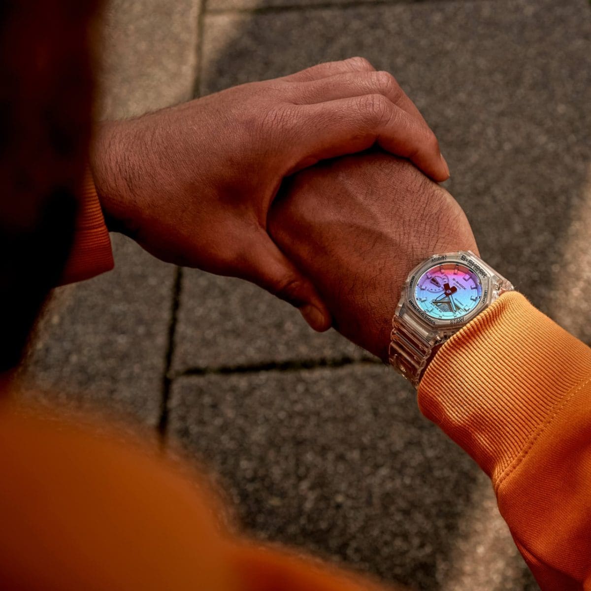 Die GA-2100SRS-7A am Handgelenk eines Mannes mit einem orangenen Pullover