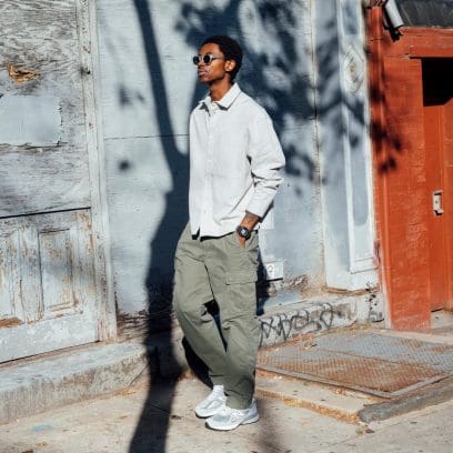 Ein Mann steht in der Sonne vor einer Hauswand und trägt ein weißes Hemd, khaki-farbene Hose, weiße Sneaker und eine Sonnenbrille. Am Handgelenk ist die GD-010-1A1 Uhr von G-SHOCK zu sehen.