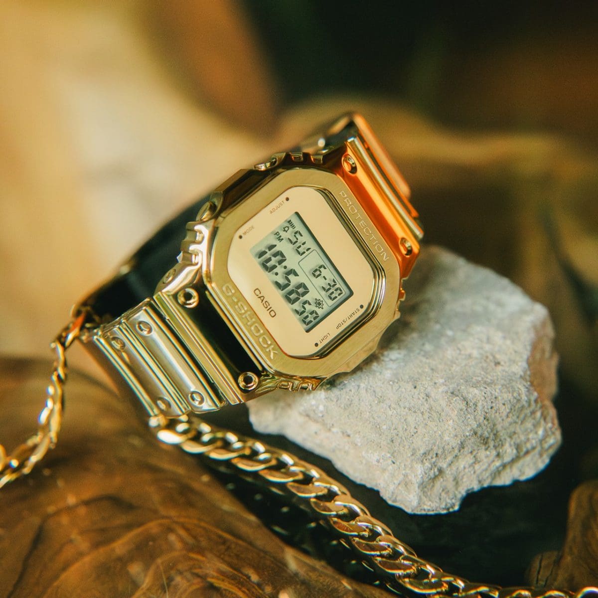 Die Digitaluhr GM-5600YMG-9 auf einem Stein neben einer goldenen Kette