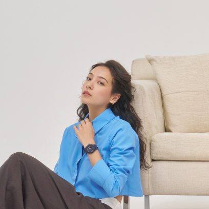 Eine Frau mit hellblauem Oberteil lehnt an einem Sofa und trägt die blaue GMA-P2100M-2A am Handgelenk