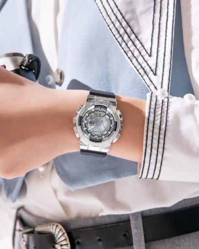 Nahaufnahme der Digital-Analoguhr von G-SHOCK mit kantigem silbernem Metallgehäuse am Handgelenk einer Frau, die eine weiße Bluse und blaue Weste trägt