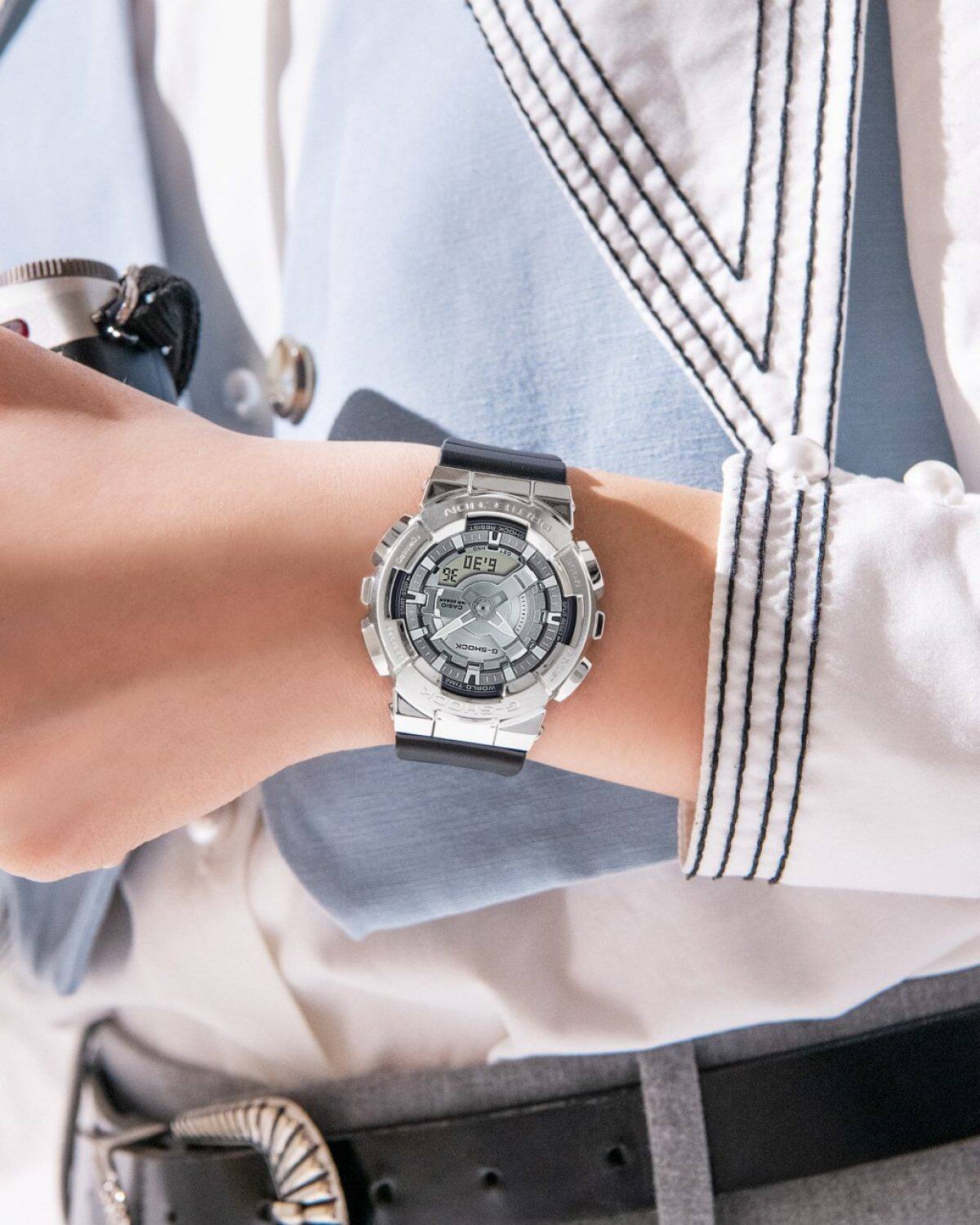 Nahaufnahme der Digital-Analoguhr von G-SHOCK mit kantigem silbernem Metallgehäuse am Handgelenk einer Frau, die eine weiße Bluse und blaue Weste trägt