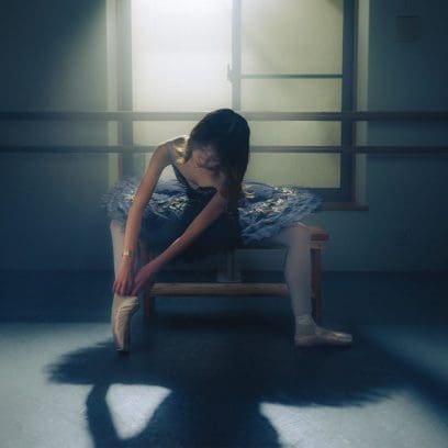 Eine Balletttänzerin sitzt auf einer Holzbank und zieht ihre Ballettschuhe an, am Handgelenk trägt sie die LA670WG-9 von CASIO.