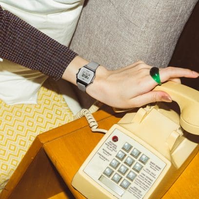 Eine Frauenhand greift zum Telefonhörer eines altmodischen Tastentelefons, am Handgelenk trägt die Frau die LA680WEL-8 Digitaluhr mit hellgrauem Lederarmband