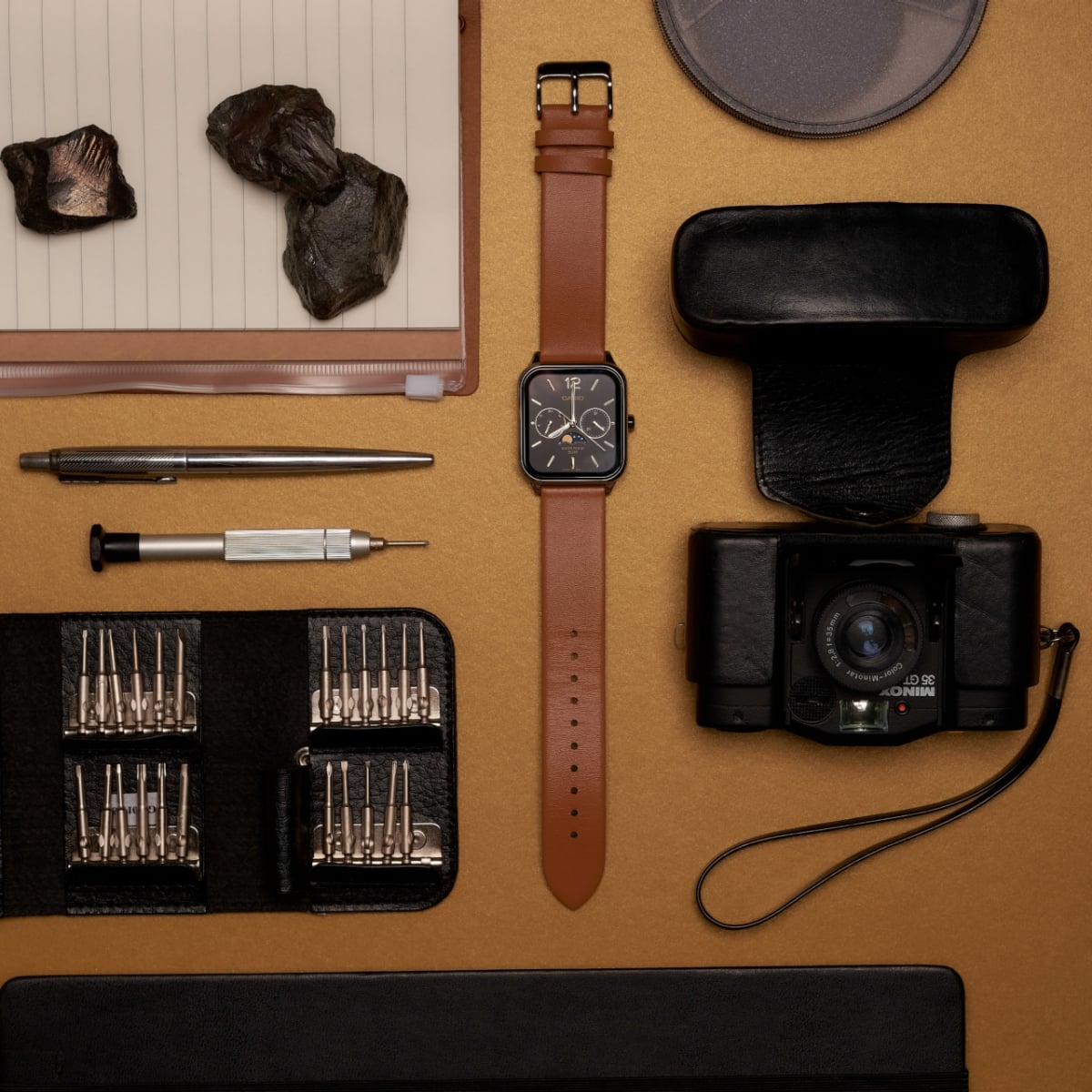 Die CASIO TIMELESS COLLECTION Armbanduhr MTP-M305L-1AV dekorativ auf einem Tisch zwischen Kamera, Steinen und Feinmechanik-Werkzeug platziert.
