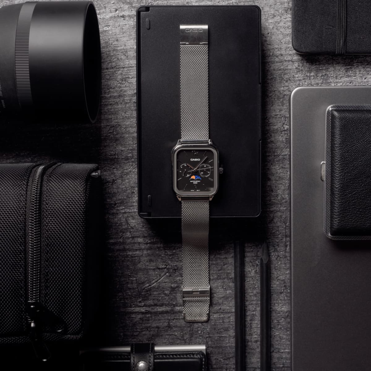 Komplettansicht der flach liegenden CASIO TIMELESS COLLECTION Armbanduhr MTP-M305M-1AV inmitten verschiedener Schreibtisch- und Fotografie-Utensilien.